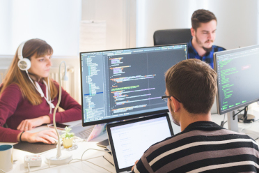 Symbolfoto Softwareentwicklung: 5 Personen in Büro schauen auf ihre Bildschirme mit Programmcodes