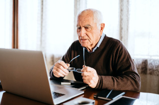 Symbolbild für Barrierefreiheit: Senior sitzt am Schreibtisch und blickt in einen Laptop.