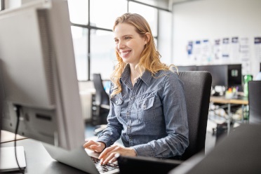Lächelnde Frau in einem Büro tippt auf die Tastatur eines Desktop-Computers.