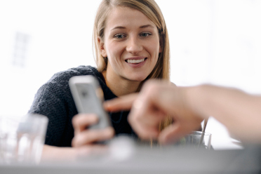 Porträt einer lächelnden Frau und ein Finger, der auf ein Handy zeigt.