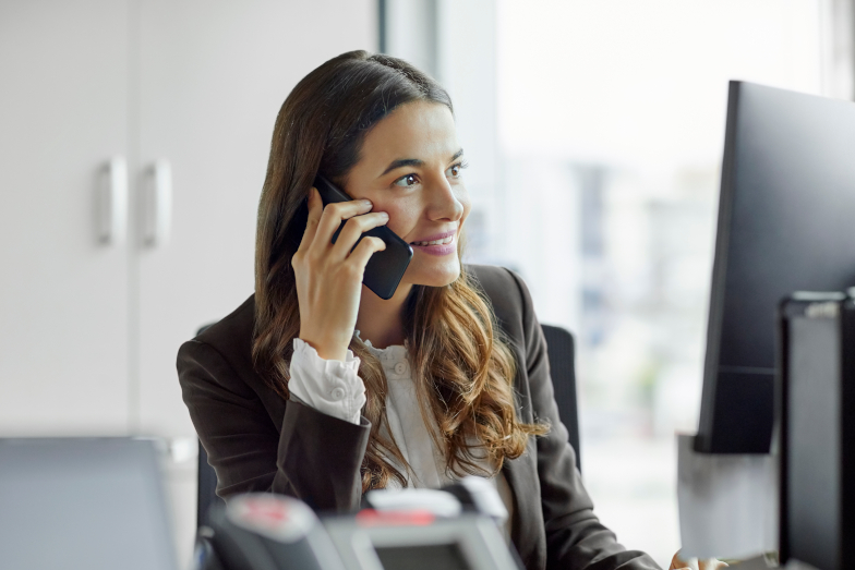 Junge Frau telefoniert an ihrem Arbeitsplatz im Büro mit einem Smartphone.