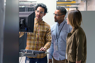 Symbolbild Jobprofil IT-Sicherheit: Eine Gruppe von Personen steht im Rechenzentrum und schaut auf einen Bildschirm.