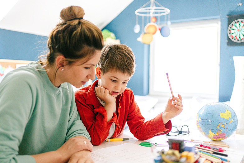 Symbolbild Vereinbarkeit von Familie, Pflege und Beruf: Mutter und Sohn sitzen am Schreibtisch und besprechen die Hausaufgaben. 