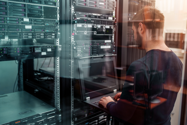 Mann arbeitet vor Serverschrank am Laptop (Quelle: AdobeStock / kiri) Mann arbeitet vor Serverschrank am Laptop