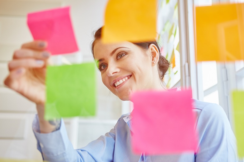 Symbolbild agile Softwareentwicklung: Junger Frau klebt Haftnotizzettel an eine Scheibe. (Quelle: Adobe Stock) Symbolbild agile Softwareentwicklung: Junger Frau klebt Haftnotizzettel an eine Scheibe.